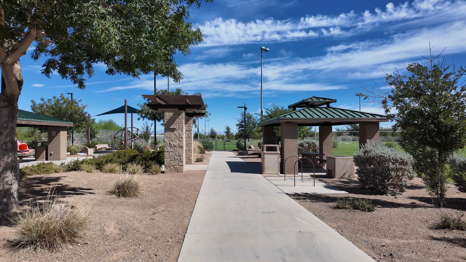Park walkway lined with desert plants leads past shaded picnic pavilions toward sports fields in Inspirada, Henderson.