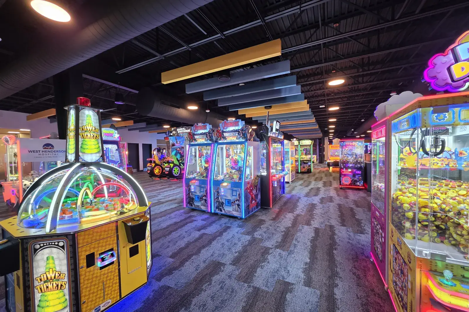 Rows of brightly lit claw and prize machines on the patterned carpet of the Henderson Sport & Social arcade