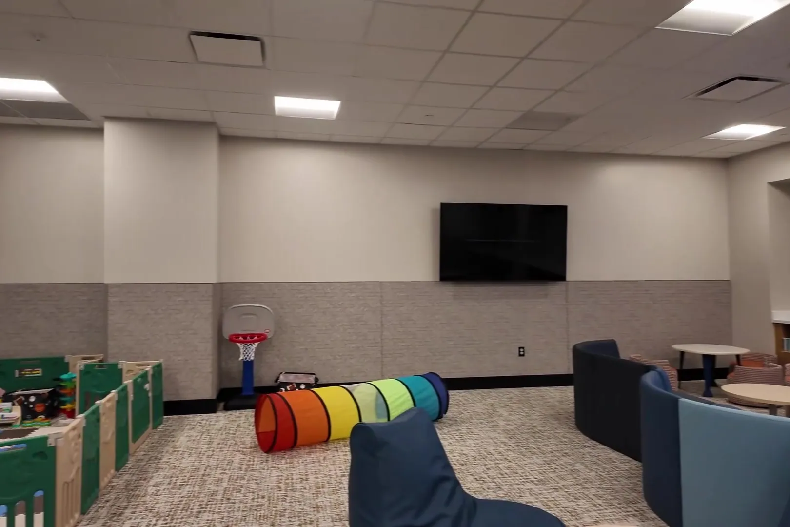 The Play Zone Child Watch room at Henderson Sport & Social, with a fenced soft-play area, a rainbow play tunnel, a toddler basketball hoop and bean bag seats