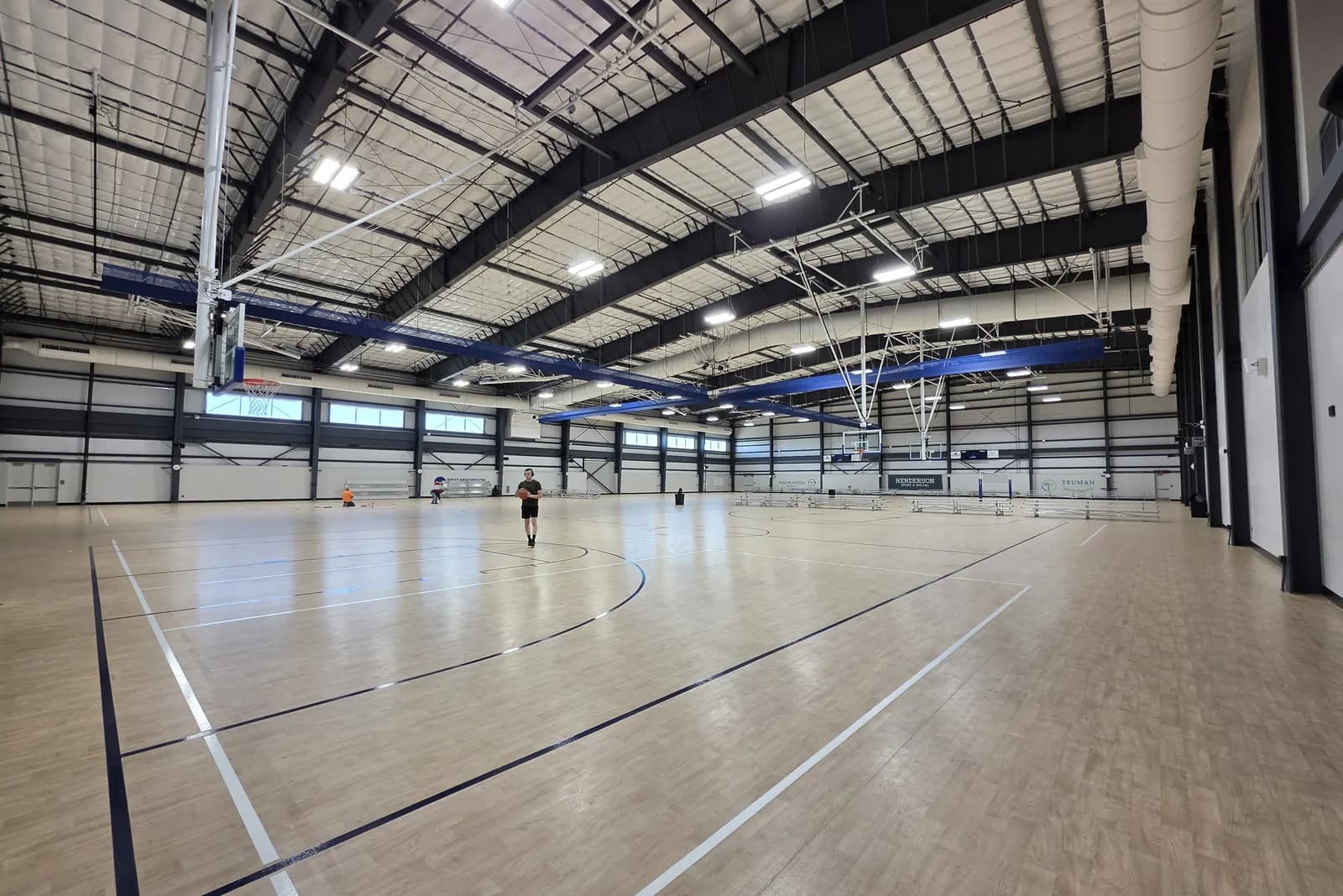 The large indoor court hall at Henderson Sport & Social, with a maple floor marked for multiple courts, retractable basketball hoops and high steel trusses