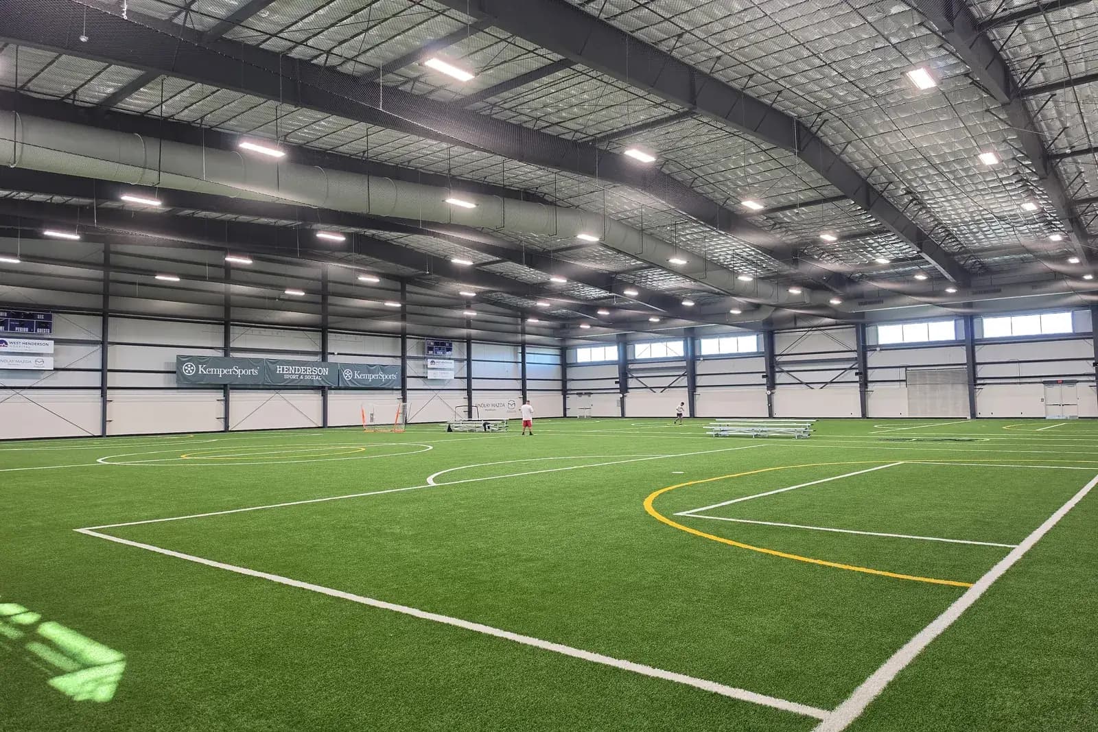 An indoor turf field at Henderson Sport & Social, with white and yellow field lines under bright high-bay lights