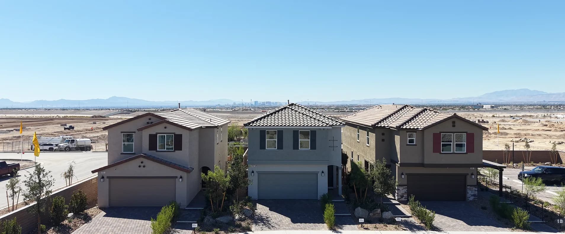 Three two-story model homes at Landings at Sandstone in North Las Vegas, with graded lots, the Las Vegas Strip, and mountains on the horizon