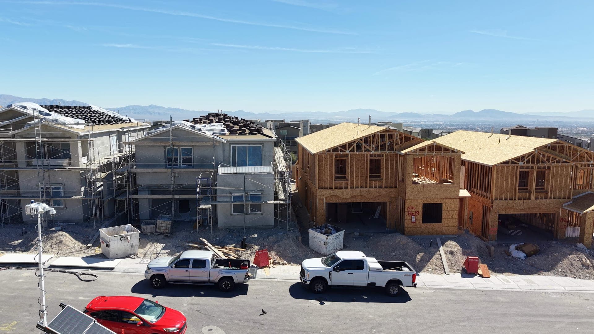 Street of new two-story homes in Summerlin at different build stages, from wood framing to stucco, with the Las Vegas Valley and mountains in the distance.