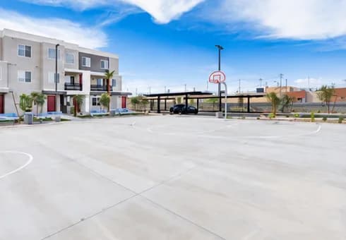 An outdoor basketball court and parking lot at Gholson Landing, with the apartment buildings visible behind it