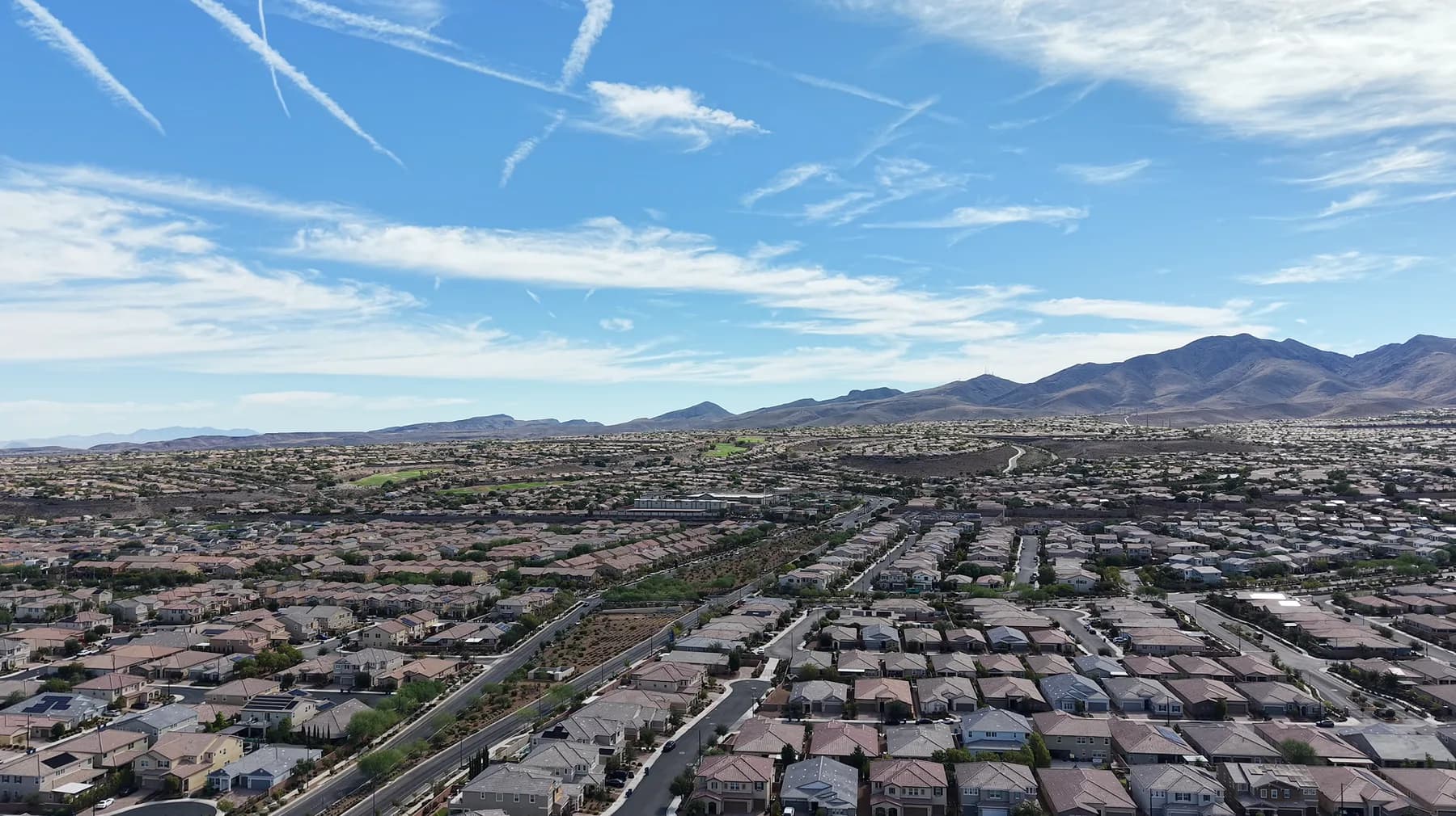 Aerial view over the rooftops of Inspirada in Henderson, streets and homes running toward the mountains in the distance.