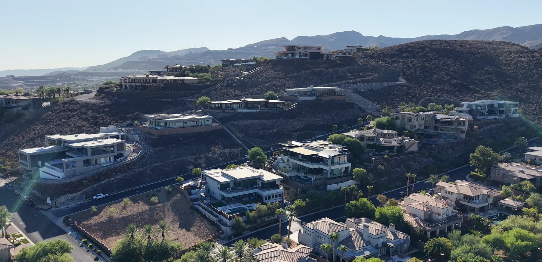 Aerial view of custom contemporary homes stepping up a hillside at MacDonald Highlands in Henderson, with graded homesites and the ridgeline behind them.