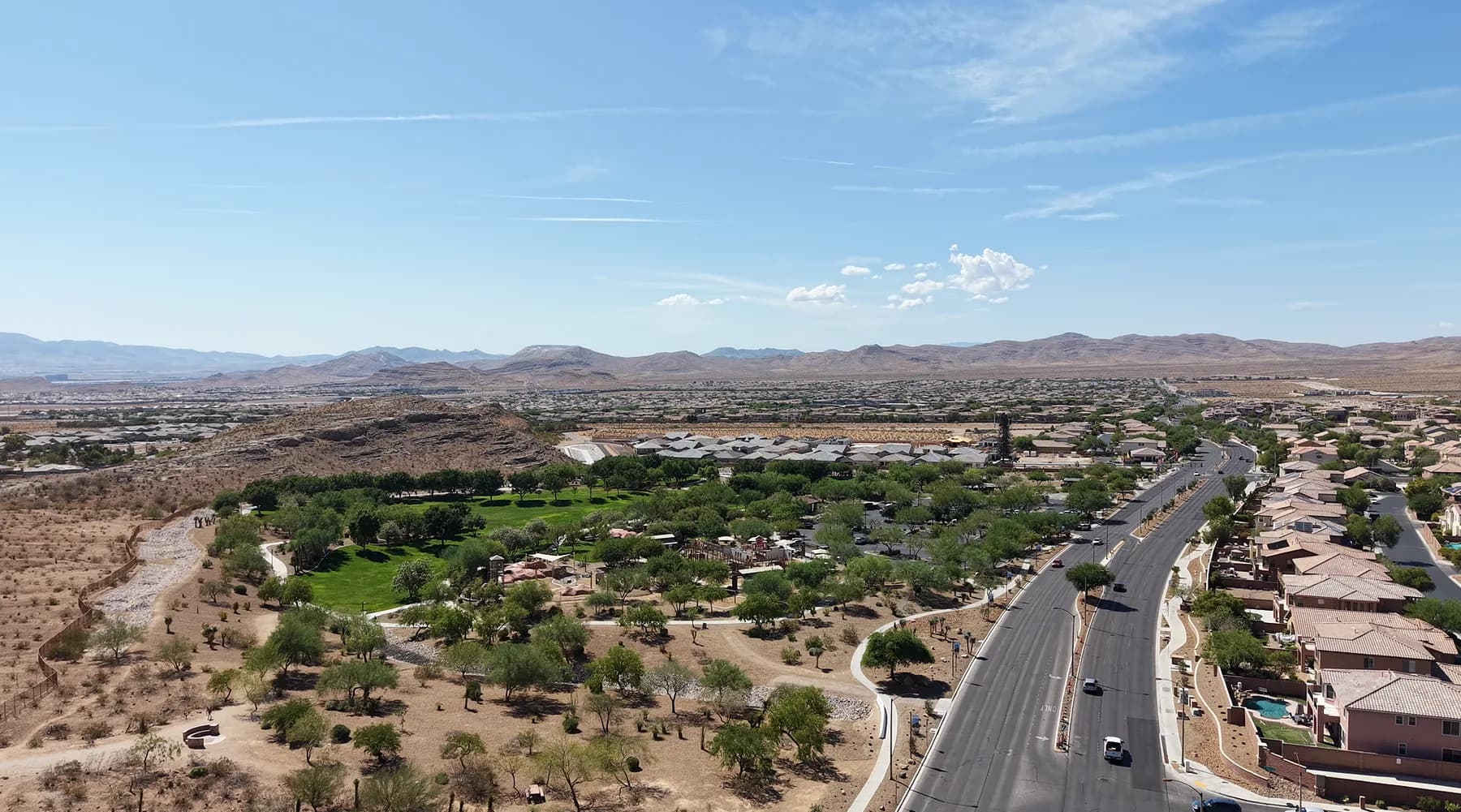 Aerial view of Exploration Peak Park in Mountain's Edge, southwest Las Vegas, green parkland beside an arterial road with homes and open desert beyond.