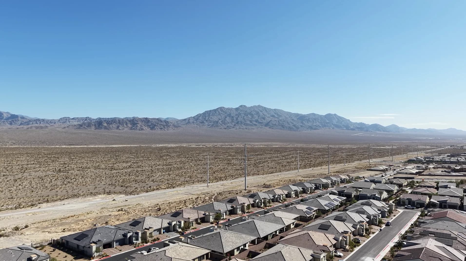 Aerial drone photo of the existing Sunstone neighborhood's rooftops in the foreground, with the vacant Monument Hills parcel stretching toward the Spring Mountains in the distance