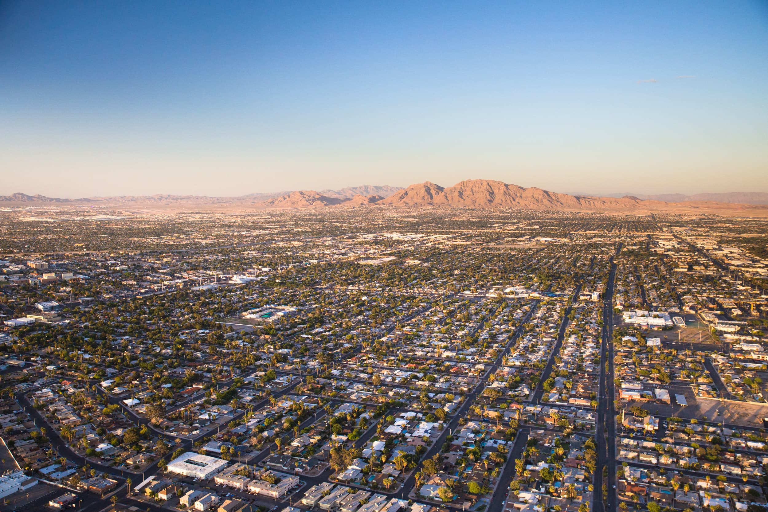 Aerial view of North Las Vegas at golden hour — the residential street grid of the northern Las Vegas Valley stretching toward the desert mountains on the horizon.
