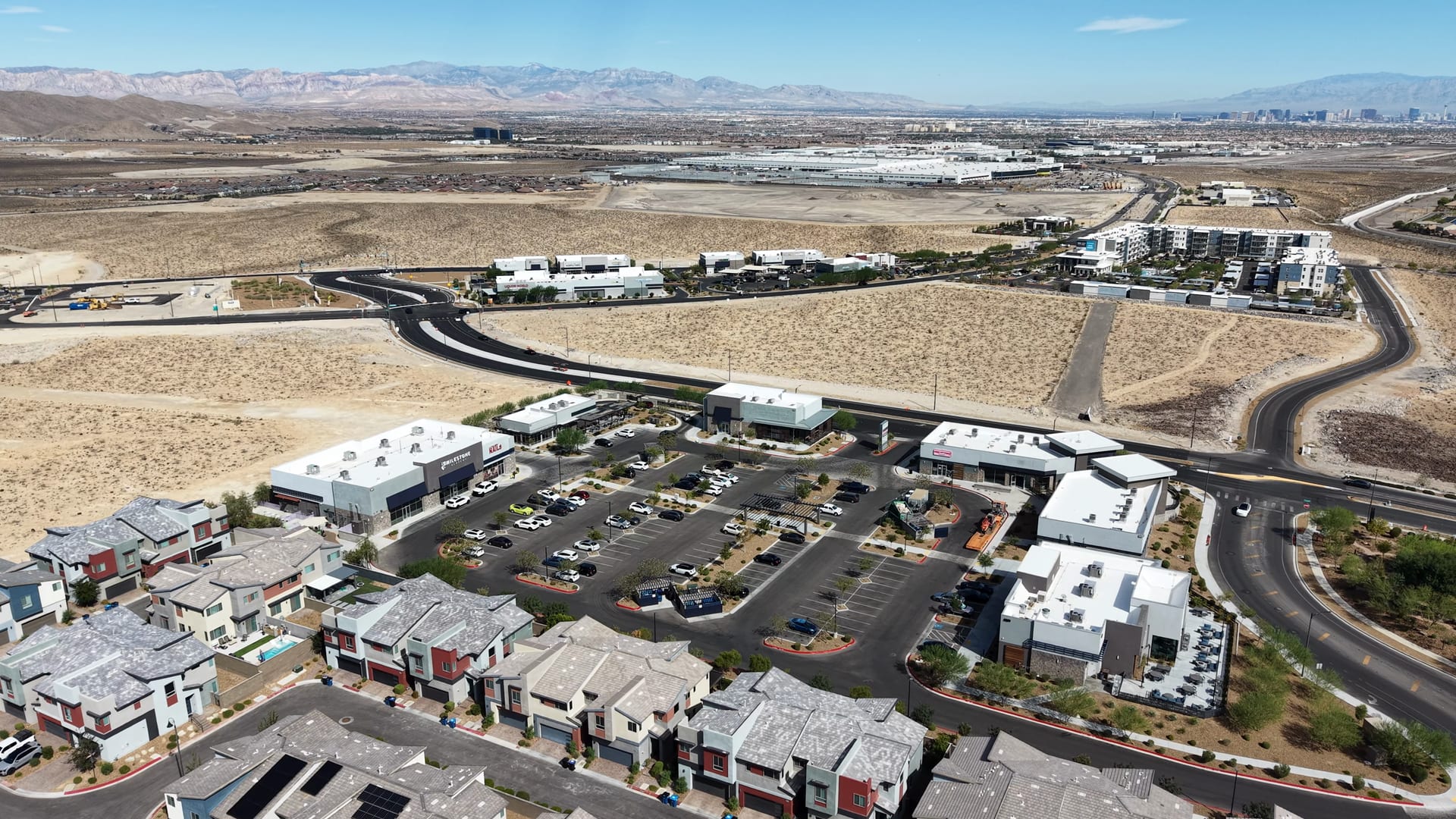 Aerial of townhomes beside a new shopping center in Inspirada, Henderson, with open desert and the distant Las Vegas Strip skyline.