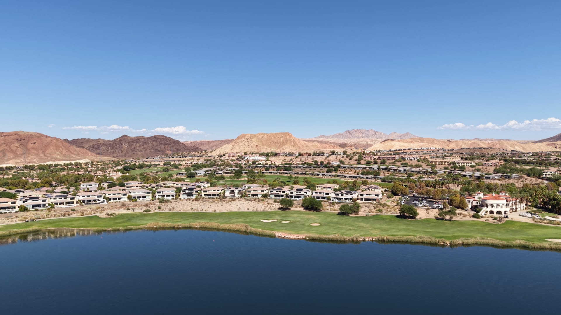 Aerial over the lake at Lake Las Vegas toward a golf fairway, rows of homes and rugged desert mountains.
