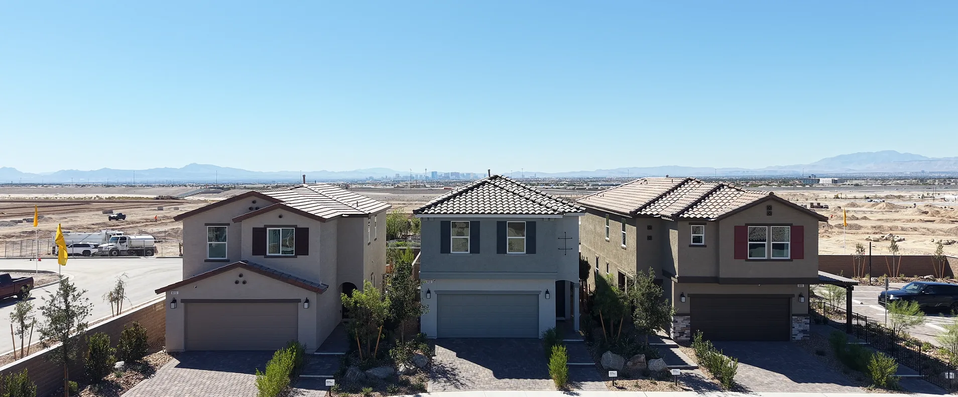 Three two-story model homes at Landings at Sandstone in North Las Vegas, with graded lots, the Las Vegas Strip, and mountains on the horizon
