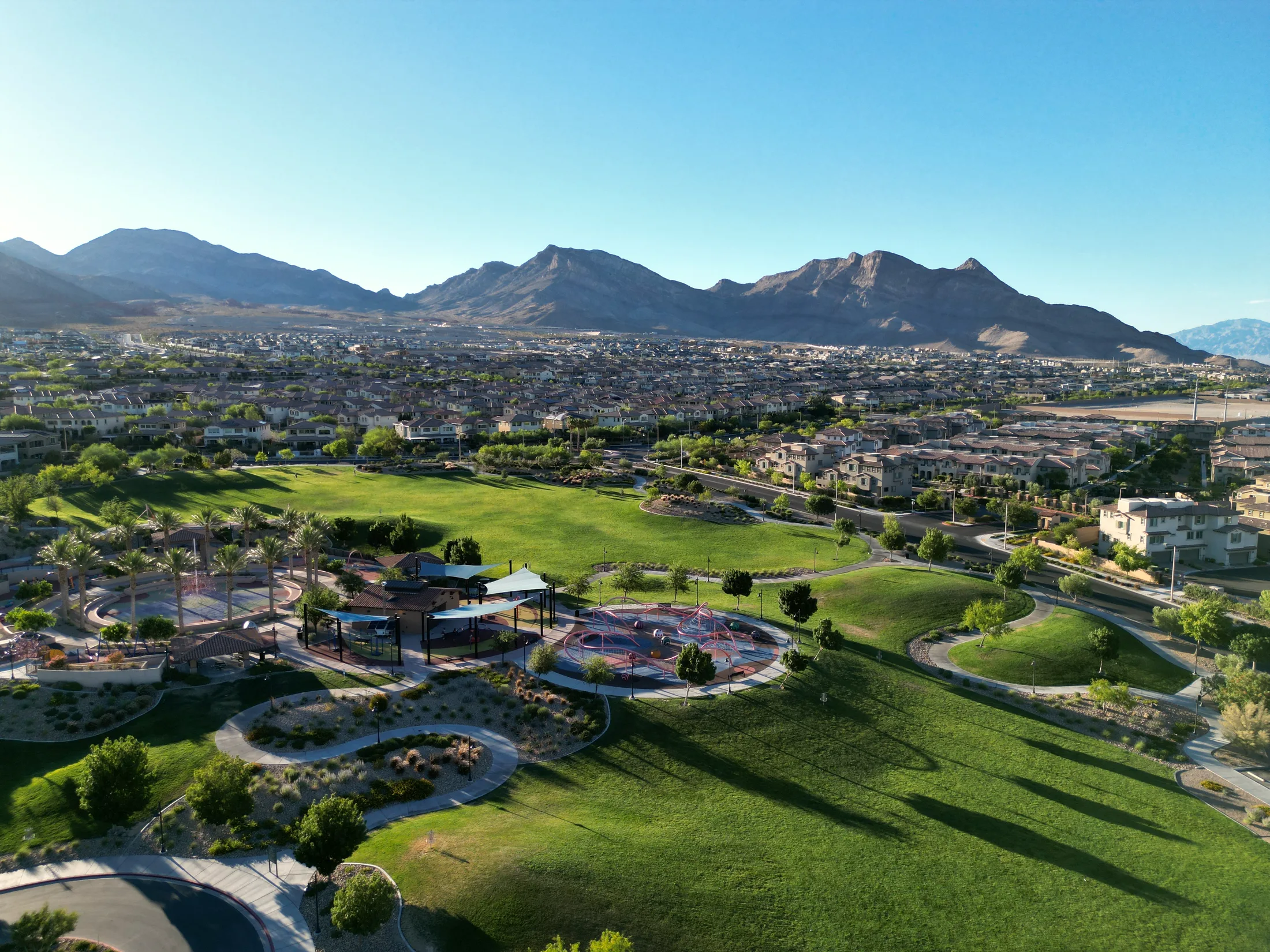 Aerial drone view over Fox Hill Park in Summerlin, the Red Rock escarpment rising beyond the rooftops.